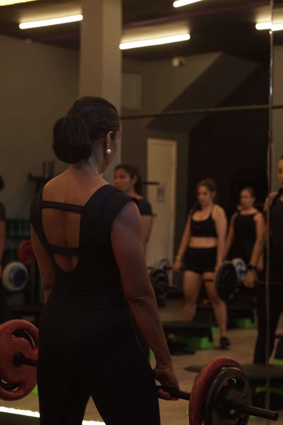 Aluna de costas segurando a barra, com a turma refletida no espelho.