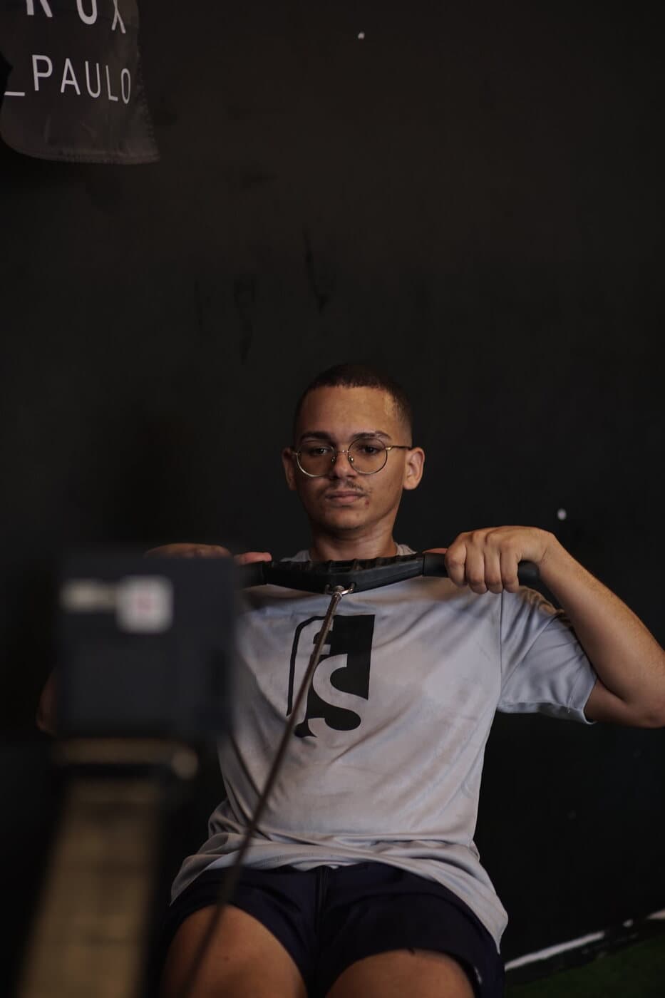 Aluno no remoergômetro, de camiseta FS Studio, no meio da remada.