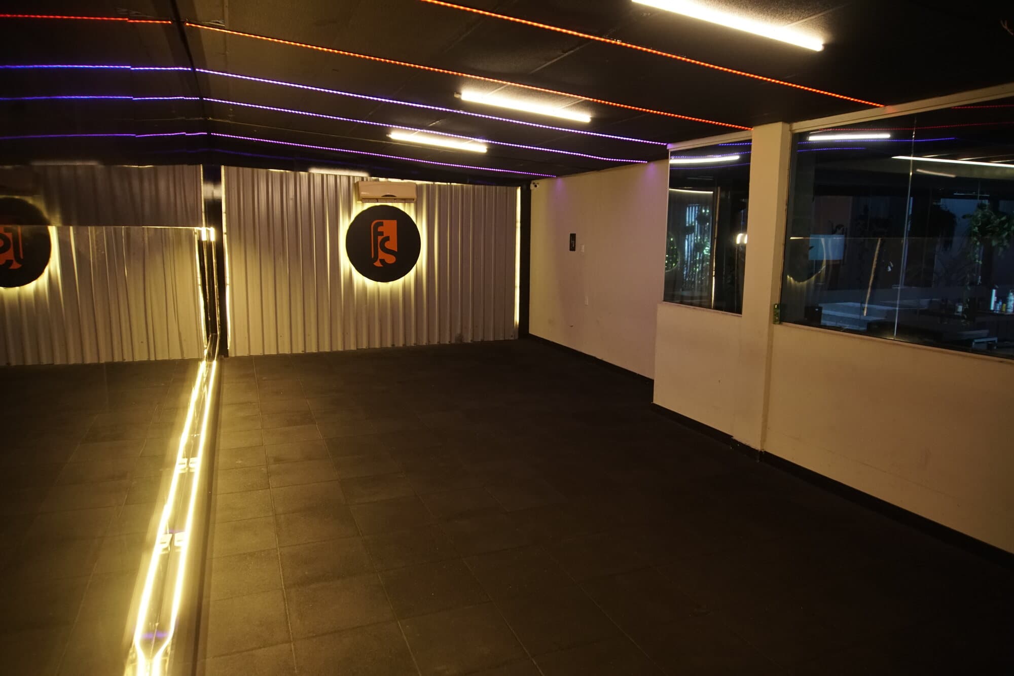 Sala de dança da FS Studio, vazia, com espelho de parede inteira e faixas de LED laranja e azul.