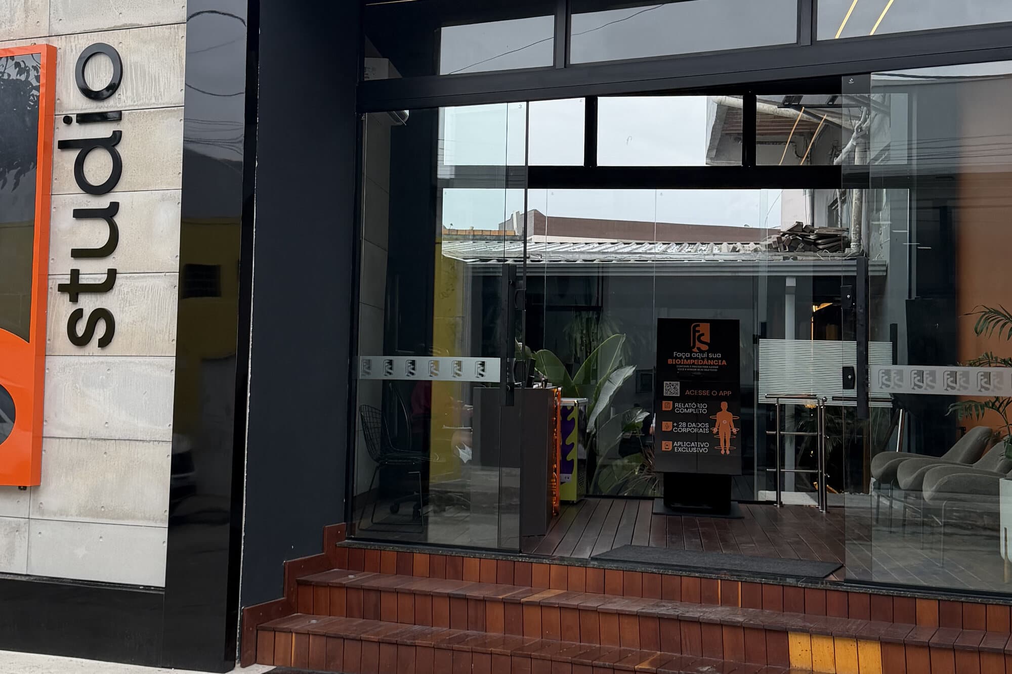 Fachada da FS Studio: logo laranja sobre a parede de pedra, letreiro studio e entrada de vidro.