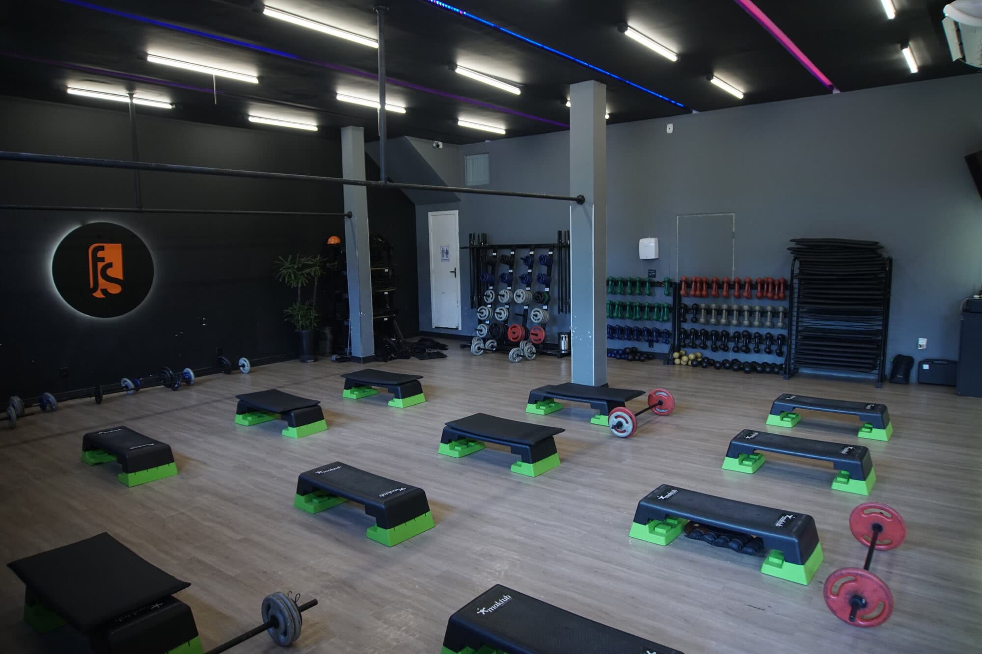 Sala funcional da FS Studio: steps e barras dispostos no piso de madeira, teto com faixas de LED coloridas.
