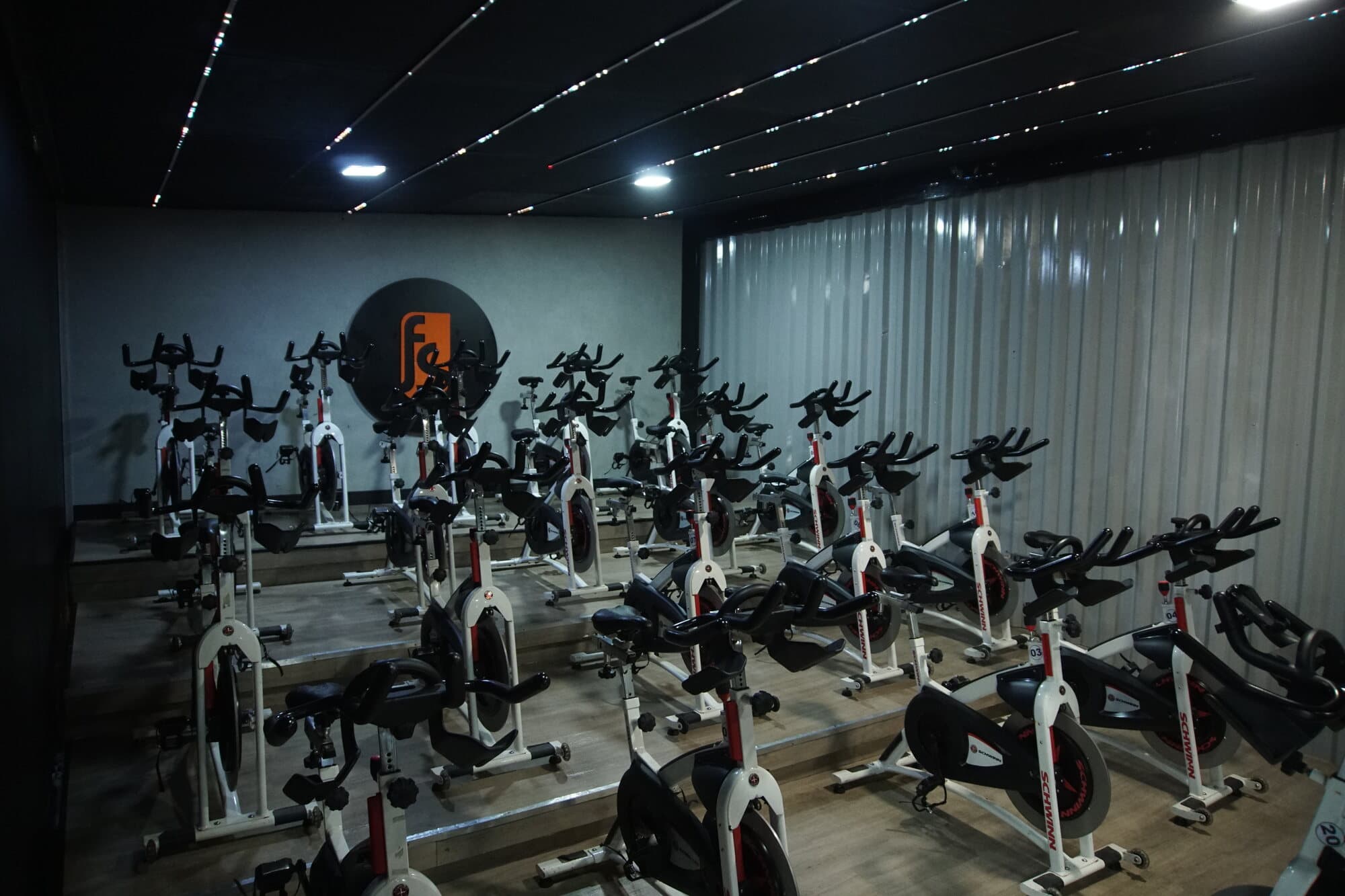 Sala de spinning da FS Studio com as bikes alinhadas sob luz baixa e o logo circular ao fundo.