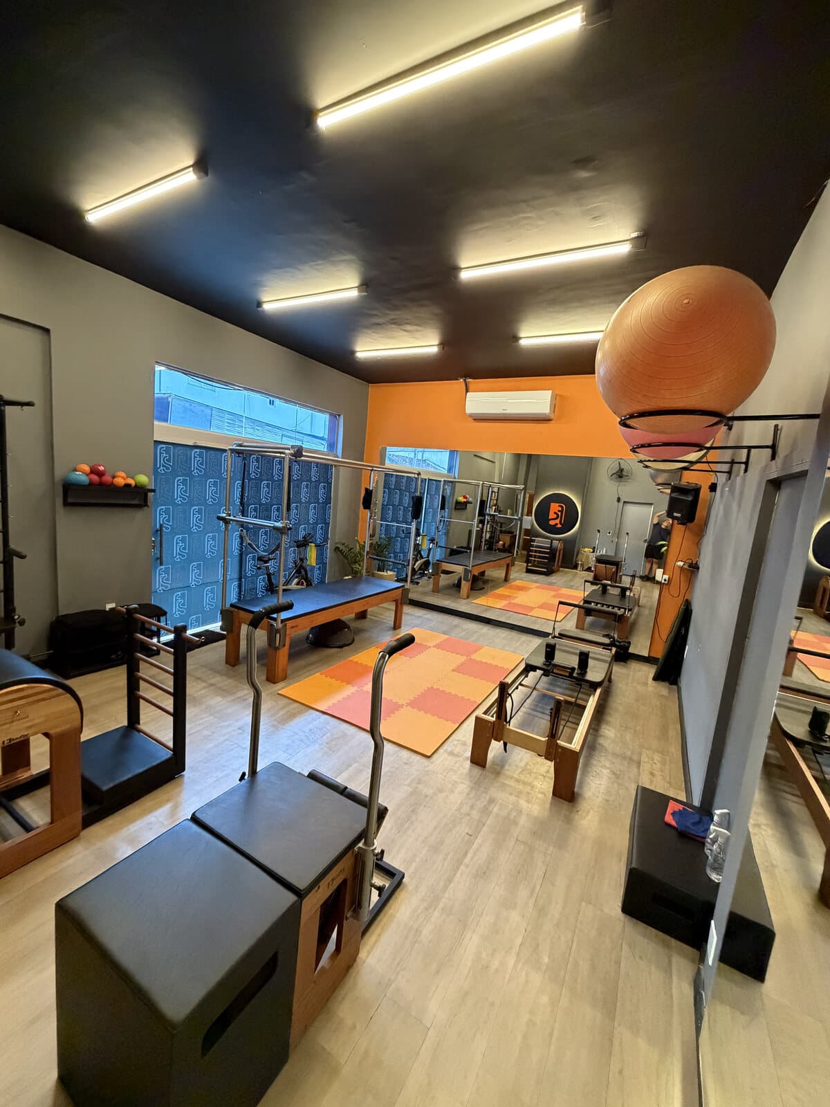 Segunda sala da FS Studio, com parede laranja, espelhos amplos e equipamentos de pilates.
